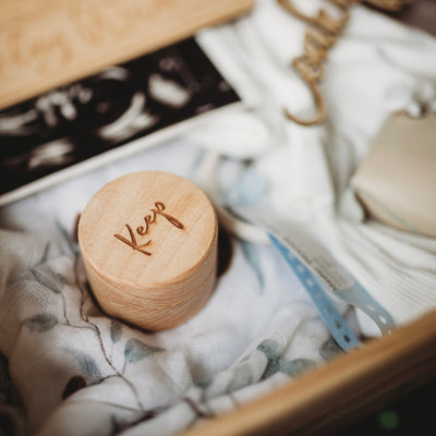 A round keepsake box saying keep on the top, in a memory box with sonogram, hospital bracelet and blanket.