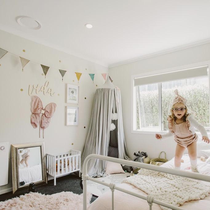 A bamboo wall name saying Vida, hanging in a little girls room, with a girl jumping on her bed.