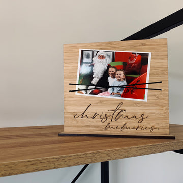 The Christmas Photo Holder, made in New Zealand and reading "Christmas memories," displays a 2017 photo of two kids with Santa. It adds festive cheer to any wooden shelf.