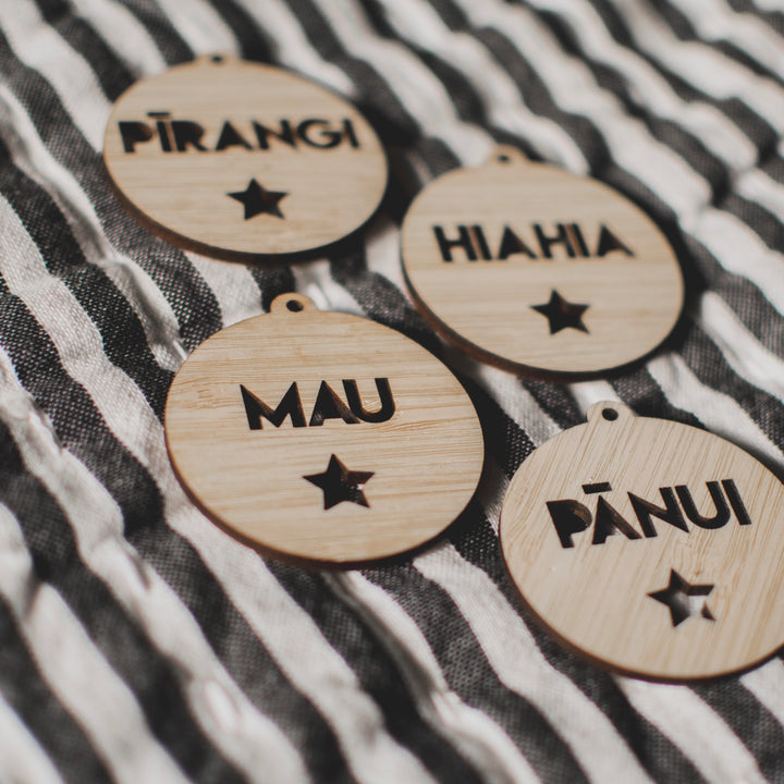 Te Reo - Want, Need, Wear, Read Tags (Unpersonalised): four round bamboo tags with cut-out stars and Te Reo words, PĪRANGI, HIAHIA, MAU, PĀNUI, arranged on black and white stripes.