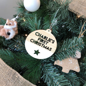 A Christmas tree wrapped with burlap ribbon is decorated with a plush cat ornament, a gingerbread-shaped decoration, and the "My First Christmas Bauble" bamboo ornament personalised with CHARLIE&