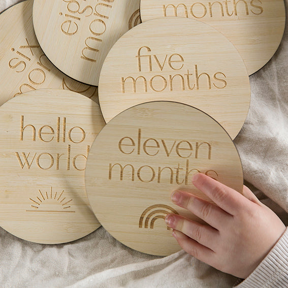 ound bamboo milestone sets. All with the months of the year and different pictures. A little hand is grabbing the one in front saying eleven months and has a rainbow engraved.